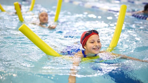 Lachende Kinder im Hallenbad auf Schwimmnudeln