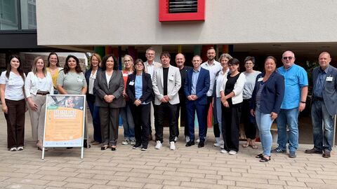 Eine Gruppe von circa 20 Personen stehen vor einem Gebäude. Vor ihnen ein Aufsteller mit der Aufschrift "Herzlich Willkommen im Cafe der kleinen Schätze".